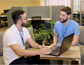 Dois colaboradores do Time Cielo conversam no escritório, com um deles digitando em notebook.